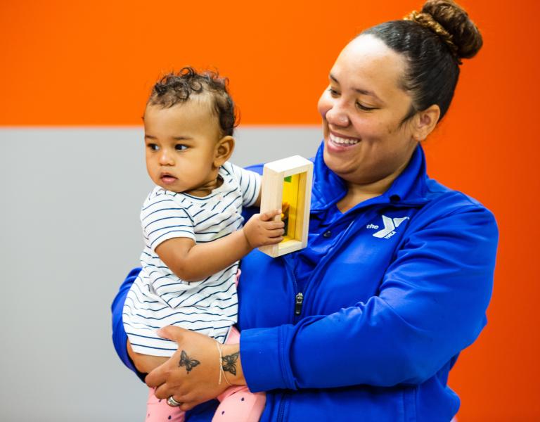 Y Infant care staff holding a baby with a block toy in hand