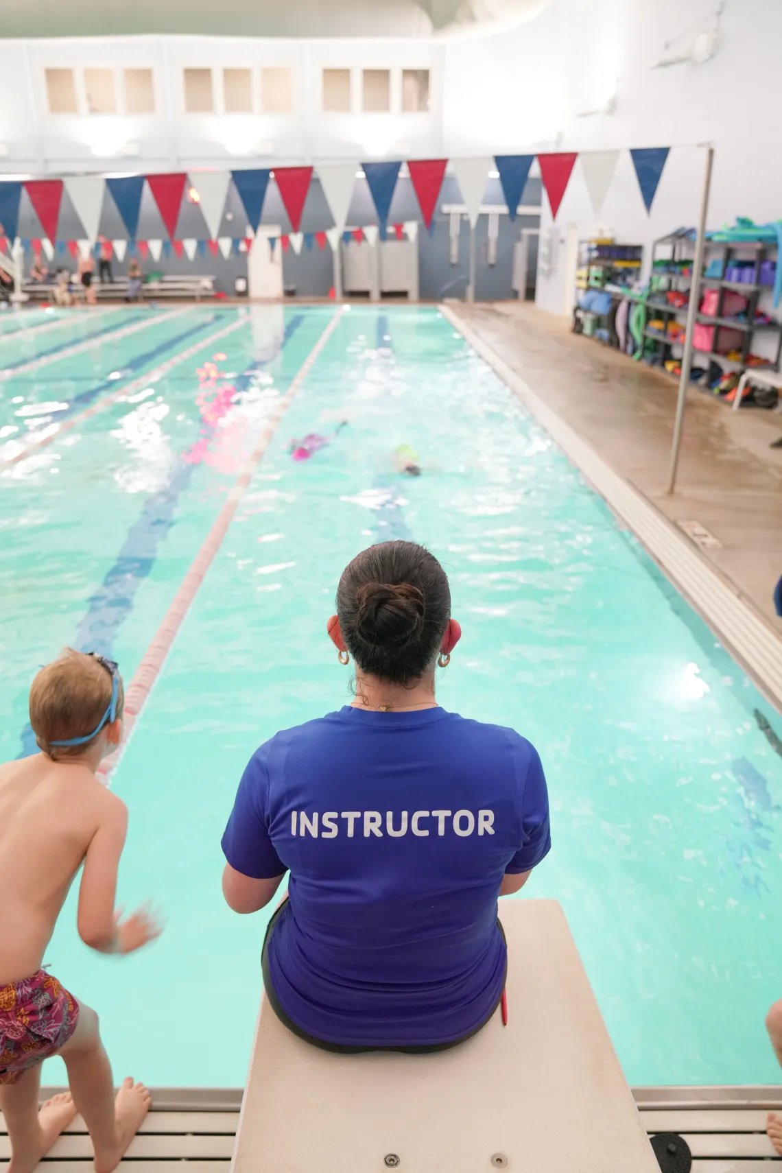 A swim instructor sits on the diving board