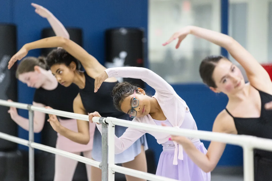 Children and youth participate in a YMCA ballet class, practicing stretches at a barre during a community arts and dance program in Pierce and Kitsap Counties.