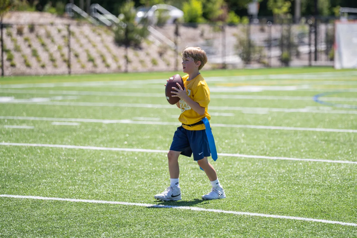 Child ready to pass a football during a YMCA youth flag football game on an outdoor field.