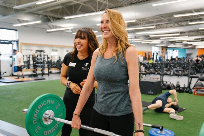 YMCA personal trainer assisting a member with a barbell exercise in the fitness center
