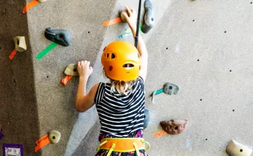Kids is focusing climbing up a rock wall in an orange harness and helmet.