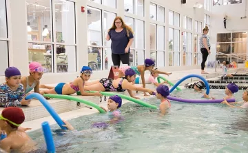 Kids at the Y Aquatics Center reach out to classmates with foam pool noodles to practice Reach, Throw, Don't Go.