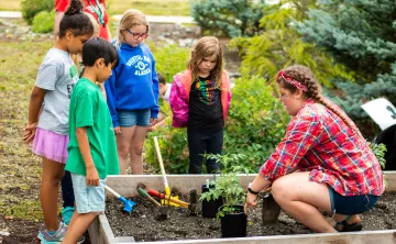 Children and an instructor gather around a planter box.