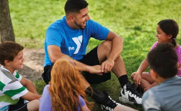 A camp counselor sits with a group of children at the Y