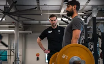 KickStart Coach Bryce watches member Benji lift weights to check for his form as part of the KickStart program. 