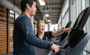 Wellness Coach Becca provides an equipment orientation on a treadmill to a member.