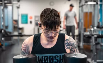A young Asian American man reflects and holds two 45 pound free weights at the University YMCA Student Center.