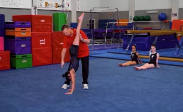 Gymnastics instructor supports a gymnast's position in a handstand and helps align their body.