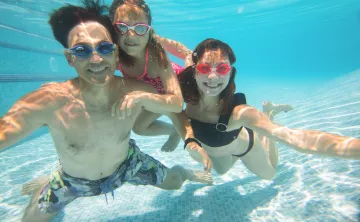 An Asian American man swims underwater with two daughters in a Y pool.
