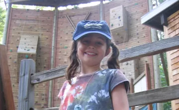 Photo of camper posing in front of the climbing wall at YMCA Camp Seymour