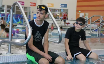 Swimming lesson participants sitting on the pool's edge while receiving instruction at the YMCA