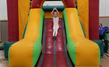 Action shot of a Healthy Kids Day participant going down the bounce house slide at the Mel Korum Family YMCA