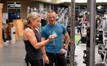 Two adults exercise at a cable machine in a gym.