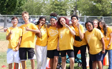 Group of YMCA summer camp participants in matching yellow camp shirts standing together outdoors on a grassy field during a summer camp activity at the YMCA of Pierce and Kitsap Counties.