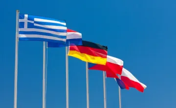 International flags representing multiple countries wave against a blue sky, symbolizing cultural exchange, global diversity, and international staff at YMCA Camp Seymour.