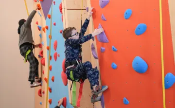 Child climbing the Liz Rocks Climbing Wall at the YMCA, building strength, confidence, and coordination through active youth recreation.
