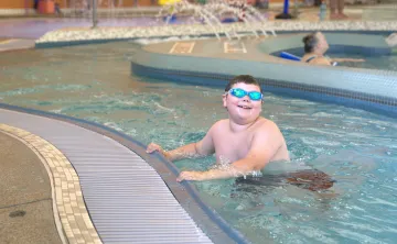 Beary wears swim goggles while holding onto the edge of the lazy river at the Gordon Family YMCA aquatic center during a YMCA swim lesson.